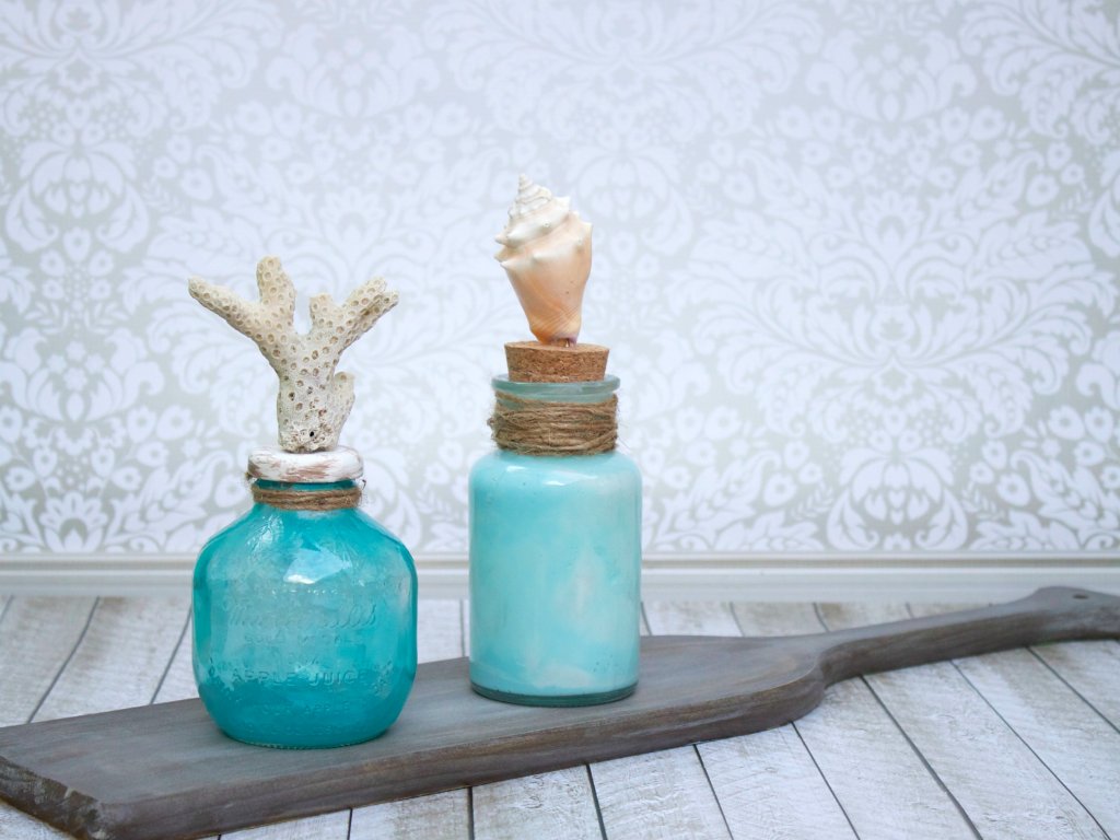 Make coastal bottle decor to bring the beach home with you. Use glass paint and souvenir shells to create beach themed home decor.