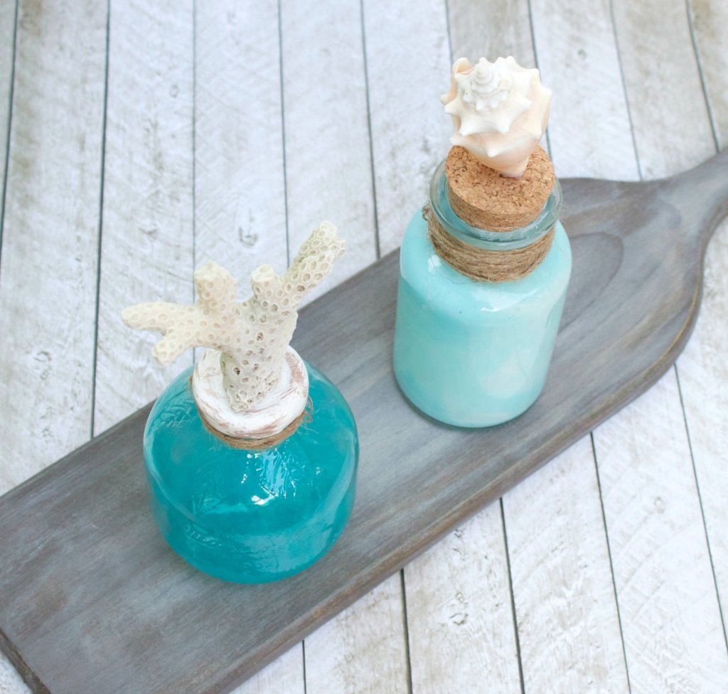 Make coastal bottle decor to bring the beach home with you. Use glass paint and souvenir shells to create beach themed home decor.