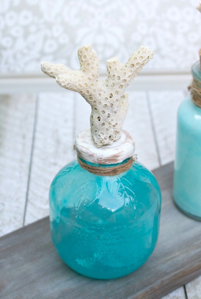 Make coastal bottle decor to bring the beach home with you. Use glass paint and souvenir shells to create beach themed home decor.