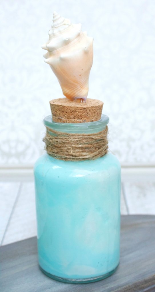 Make coastal bottle decor to bring the beach home with you. Use glass paint and souvenir shells to create beach themed home decor.